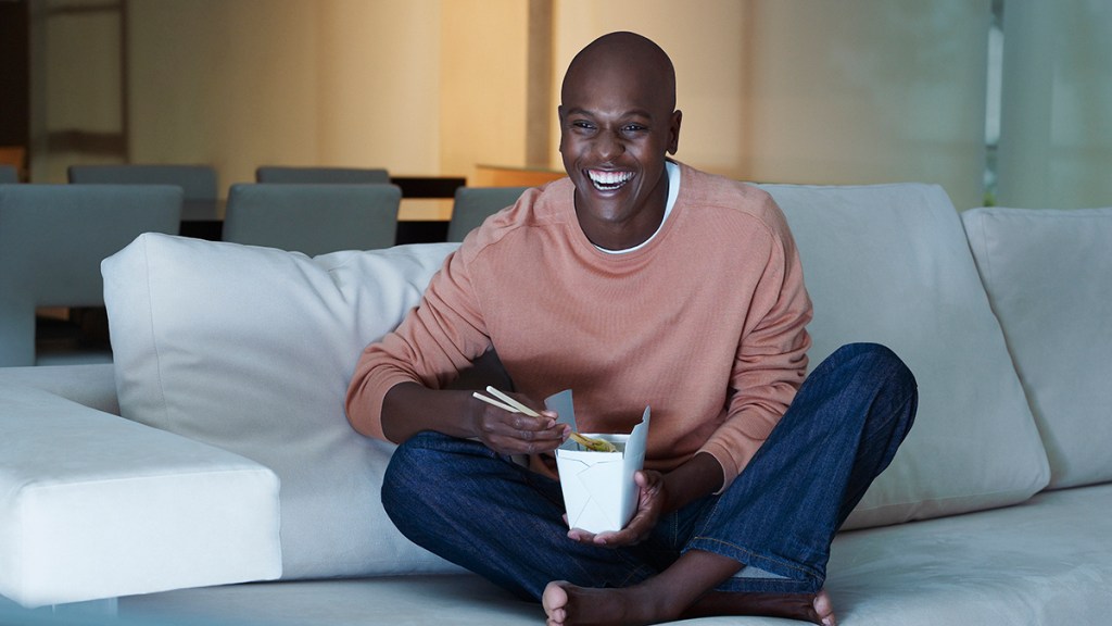 Man eating Chinese food watching television